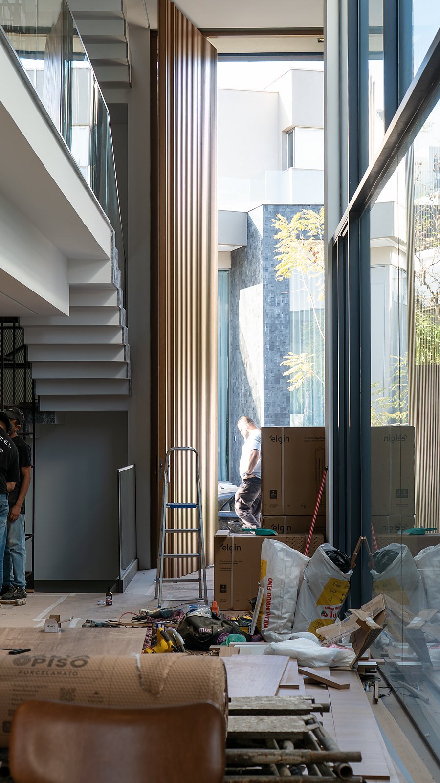 Pé-direito duplo visto do hall, com o painel ripado e a escada em balanço